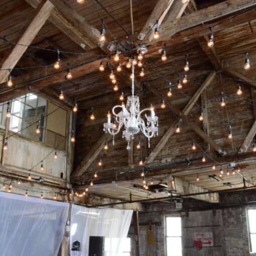 String Lights hanging in a circular pattern with a chandelier and white sheer curtains between the center columns at The Greenpoint Loft.