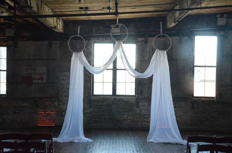 Sheer curtains hanging in a M-Shaped pattern with three white rings for the wedding ceremony.