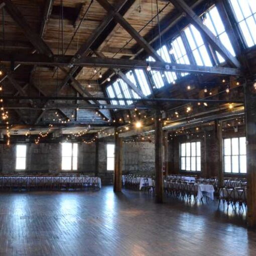Warm White String Lights hanging in parallel lines between the six center columns for a wedding in the main room at The Greenpoint Loft.