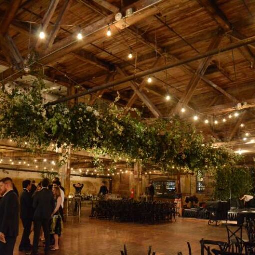 Warm White String Lights hanging in parallel lines between the six center columns for a wedding in the main room at The Greenpoint Loft.