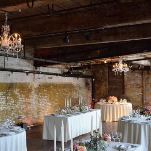 Crystal chandeliers are hanging under the lower ceiling area on the sides of the main floor at The Greenpoint Loft for a wedding.