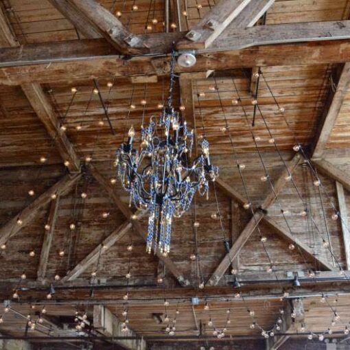 A chandelier and string lights in two V-shapes with a large swoop leading up to a center point above the ceiling of the main floor at The Greenpoint Loft.