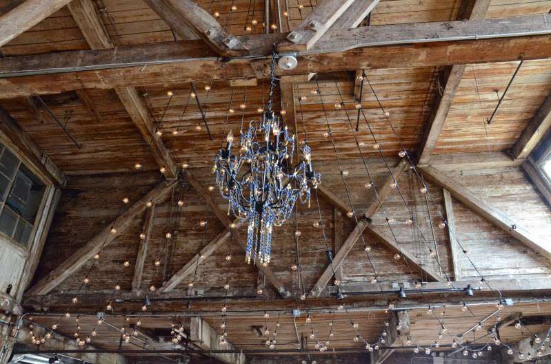 A chandelier and string lights in two V-shapes with a large swoop leading up to a center point above the ceiling of the main floor at The Greenpoint Loft.