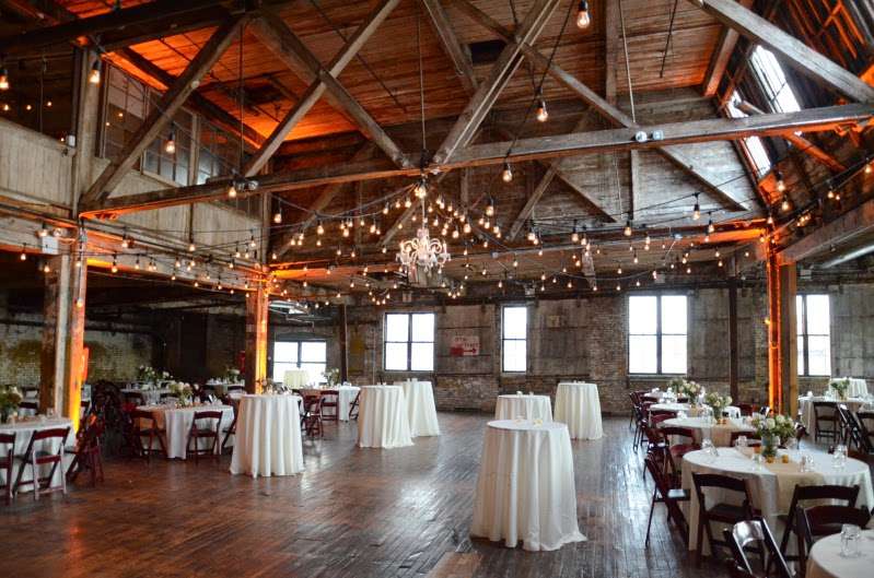 String Lights hanging in a circular pattern with a chandelier between the center columns and Up-lights for a wedding at The Greenpoint Loft.
