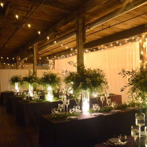 Warm White String Lights are hanging in a zigzagging pattern under the lower ceiling area on the main floor for a wedding at The Greenpoint Loft.