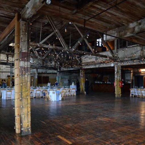 String lights are hanging in a zigzagging pattern with additional string lights wrapped around the six center columns for a wedding in the main room at The Greenpoint Loft.