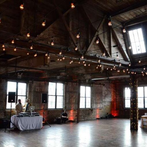 String lights are hanging in a zigzagging pattern with additional string lights wrapped around the six center columns for a wedding in the main room at The Greenpoint Loft.