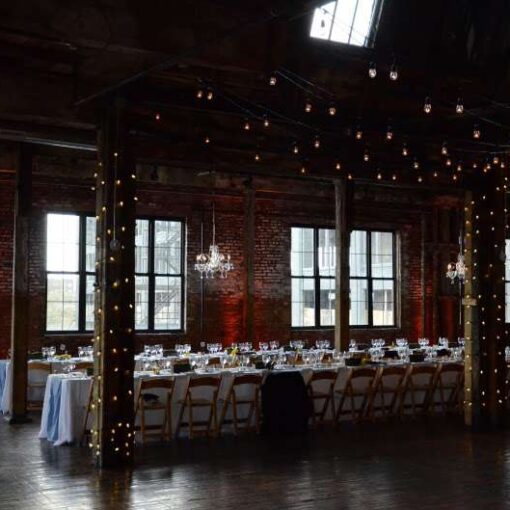 string lights wrapped around the six center columns and chandeliers for a wedding in the main room at The Greenpoint Loft.