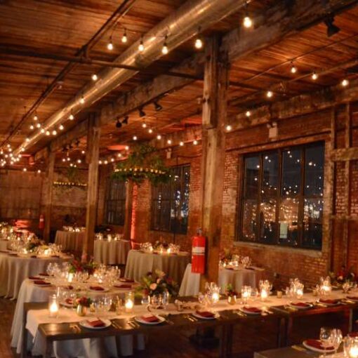 Warm White String Lights hanging in parallel lines under the lower ceiling area with a two circular votive chandeliers for a wedding in the main room at The Greenpoint Loft.