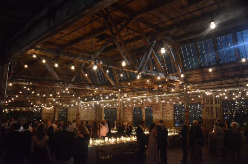 Warm White String Lights hanging in parallel lines between the six center columns for a wedding in the main room at The Greenpoint Loft.