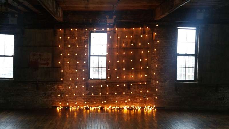 String Lights suspended vertically as a backdrop behind ceremony for a wedding at The Greenpoint Loft located in Brooklyn, New York