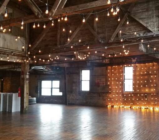 String Lights suspended vertically as a backdrop behind ceremony and overhead on the main floor for a wedding at The Greenpoint Loft located in Brooklyn, New York
