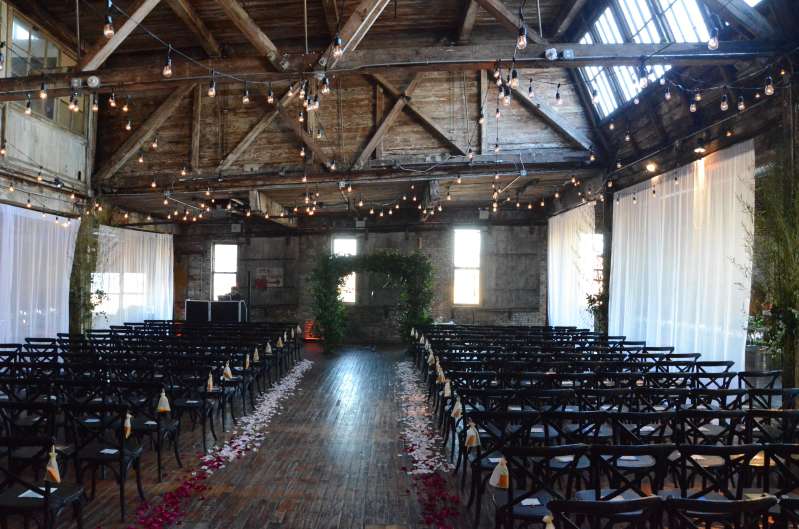 String Lights with S14 Bulbs are hanging under the high ceiling area between the six center columns on the main floor at The Greenpoint Loft. Also white Sheer Curtains for partitioning the ceremony area.