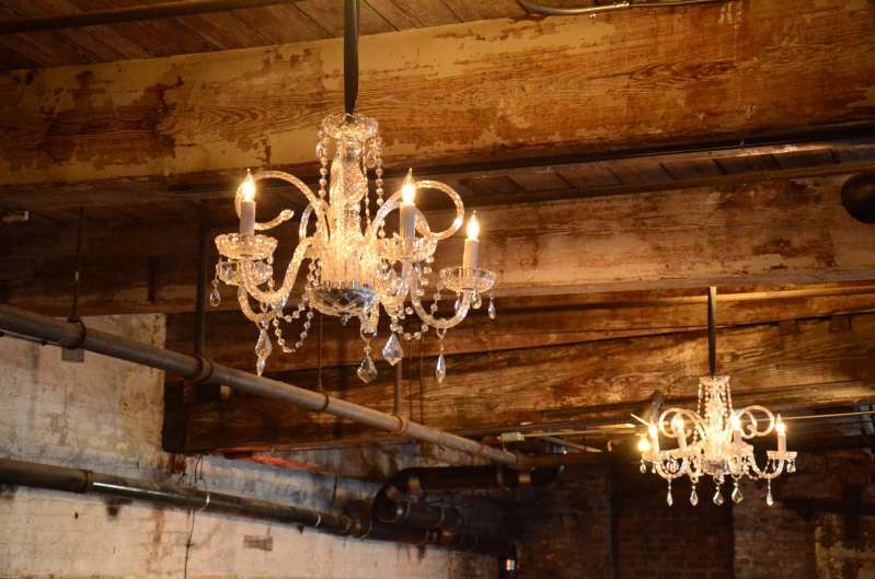 Crystal chandeliers are hanging under the low ceiling area on the main floor for a wedding at The Greenpoint Loft.