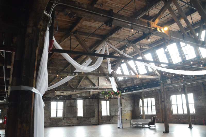 White sheer drapes hanging in an X-Shaped pattern under the high ceiling area of the main floor with String Lights at The Greenpoint Loft.