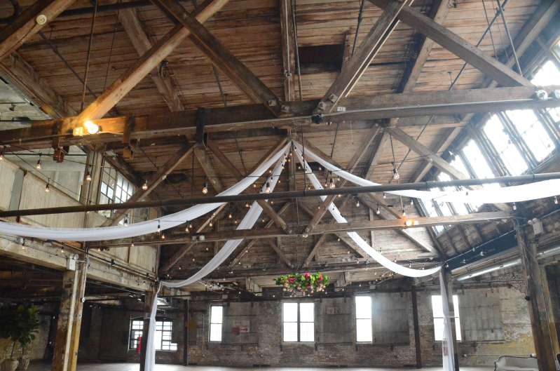 White sheer drapes hanging in an X-Shaped pattern under the high ceiling area of the main floor with String Lights at The Greenpoint Loft.
