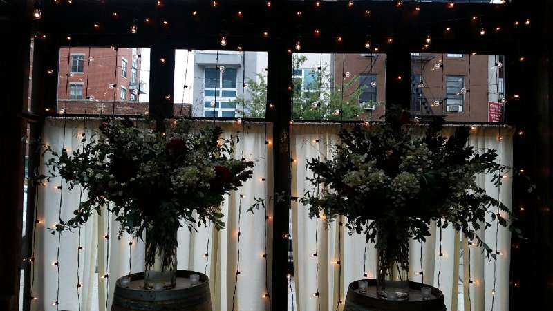A vertical curtain of string lights hanging against the windows for a wedding in the atrium at The Brooklyn Winery.
