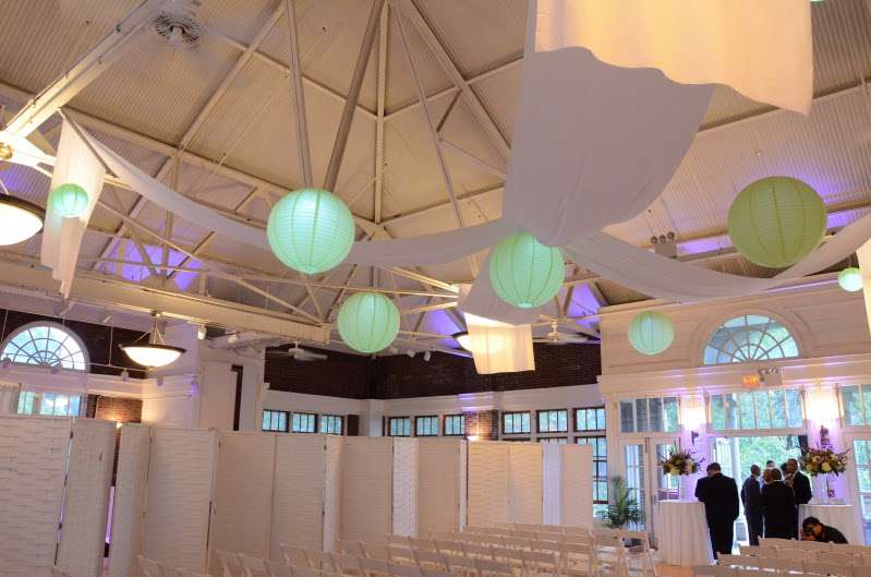 Lime Green Paper Lanterns hanging at various heights, size, with a decorative LED light inside at The Prospect Park Picnic House.  Also, Lavender Wireless LED Up-Lights around the perimeter of the room inside The Prospect Park Picnic House.  Also, white drapes hanging in a X-shaped pattern between lanterns.