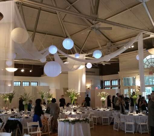 Pin-Spots for floral centerpiece at each dinner table. Also, Pin-Spots on the bar and cake table.  In addition, white sheer drapes in a X-Shape over the dinner tables. Finally, Paper Lanterns each with a decorative LED Light hanging inside The Prospect Park Picnic House.