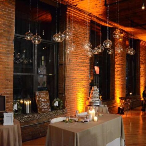 Sting Lights with S14 bulbs hanging above the center area of The Dumbo Loft between center columns.  7in Hanging Glass Ball Votive Candle Holders over ceremony area.  Grape vine orbs hanging over the center area / dance floor between columns.  Also, Up-Lights in Amber around the perimeter of the main room.