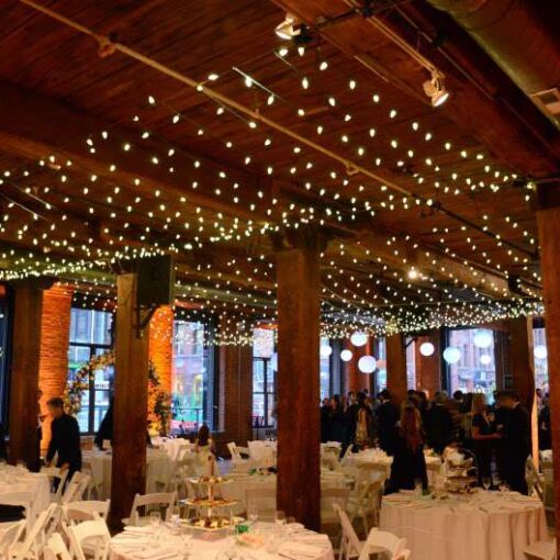 Mini-LED string lights hanging in multiple parallel lines as a canopy at The Dumbo Loft.  Also, Paper Lanterns hanging on the side of the main room. Finally, up-lights setup around the perimeter walls.