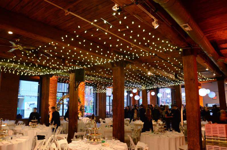 Mini-LED string lights hanging in multiple parallel lines as a canopy at The Dumbo Loft.  Also, Paper Lanterns hanging on the side of the main room. Finally, up-lights setup around the perimeter walls.