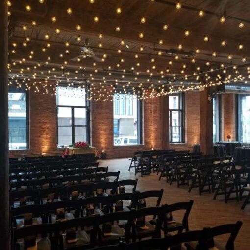 A canopy of String Lights w/ Round G50 Bulbs hanging between the center columns at The Dumbo Loft. Also, Up-Lights at the base of each brick column between the windows at The Dumbo Loft.