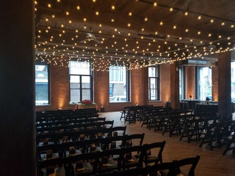 A canopy of String Lights w/ Round G50 Bulbs hanging between the center columns at The Dumbo Loft. Also, Up-Lights at the base of each brick column between the windows at The Dumbo Loft.