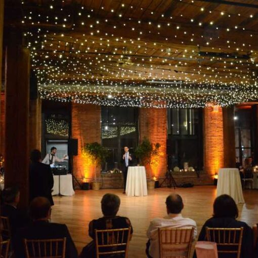 A canopy of Twinkle Lights hanging between center columns at The Dumbo Loft. Also, Up-Lights are set at the base of each column between windows.