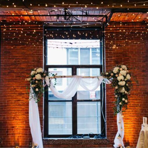A canopy of Twinkle Lights hanging between center columns at The Dumbo Loft. Also, Up-Lights are set at the base of each column between windows.