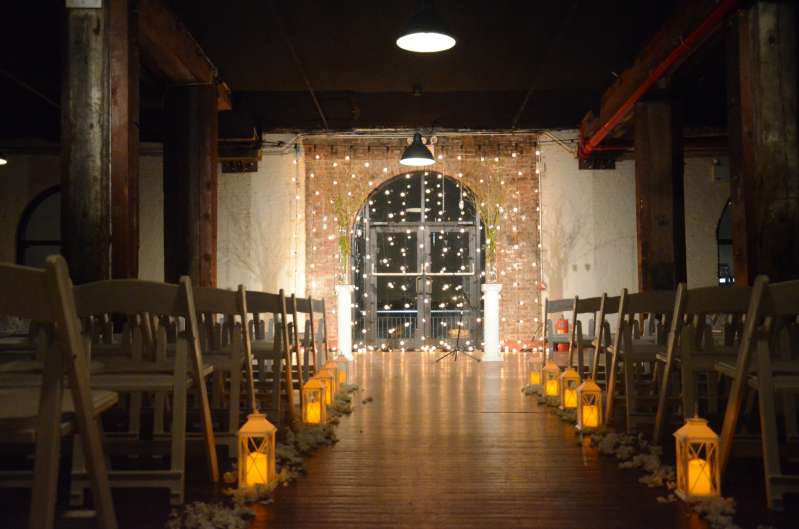 String Lights hanging vertically on 1st floor as a backdrop behind the ceremony with a spotlight on the ceremony at The Liberty Warehouse.