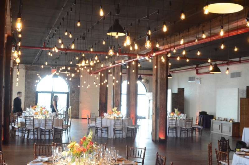 Pendant Lamps hanging between the center columns above the full length of The Harbor Room at The Liberty Warehouse. Also, Up-Lights around the perimeter wall. In addition, Up-Lights at the base of each center column.