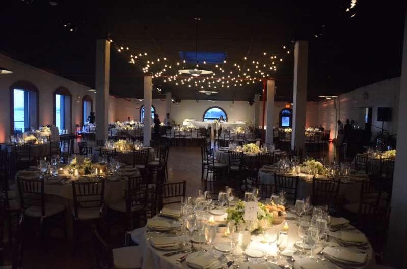 Pin-Spot is highlighting the tables and up-lights placed around the perimeter wall and string lights hanging above the dance floor.