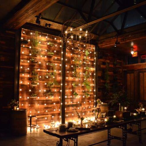 String lights hanging vertically against the main wall in The Atrium at The Brooklyn Winery for their Harvest Party. Also, round Orb Chandeliers hanging in The Atrium at The Brooklyn Winery for their Harvest Party.