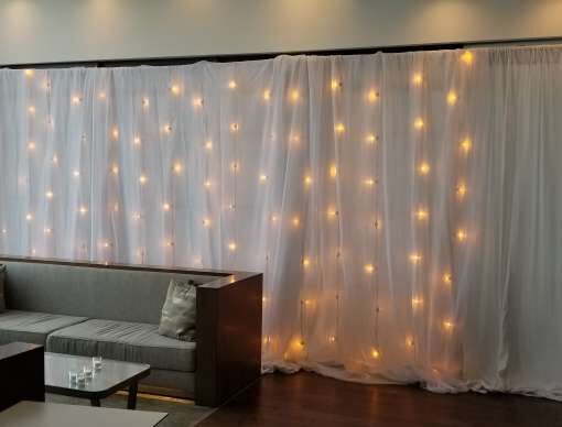 Vertical String Lights w/ white sheer and non-sheer drapes hanging against a wall at The RoofTop at Exchange Place.