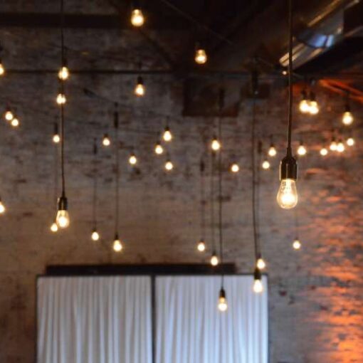 String Lights with Pendant Lamps and warm white Bulbs hanging overhead in the main room at The Green Building. Also, Amber Up-Lights setup along the inside walls of the main room at The Green Building.