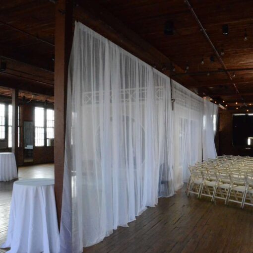 White Sheer Curtains hanging across the width of the 4th floor at a temporary partition during cocktail hour at The Metropolitan Building.