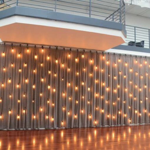 A vertical curtain of string lights hanging as a backdrop against rear dance floor wall at The Tribeca Rooftop.