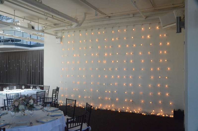 String Lights hanging vertically as a backdrop against the wall next to rear bar at The Tribeca Rooftop.