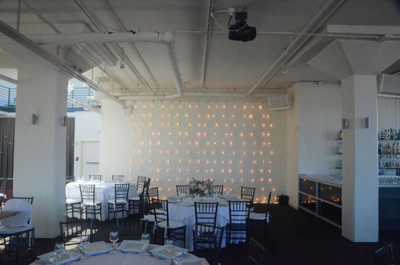 String Lights hanging vertically as a backdrop against the wall next to rear bar at The Tribeca Rooftop.
