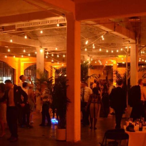 String Lights hanging above the dancefloor with amber Up-Lights around the perimeter walls for a wedding at The Lightbox in The Bronx, NY.