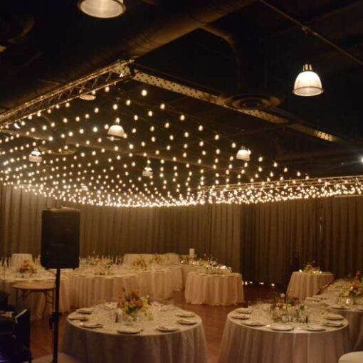 Crystal Chandeliers hanging over dinner tables along with a canopy of String Lights with round G50 bulbs hanging above the dance floor for a wedding at The Lighthouse at Chelsea Piers located at Pier 61 in New York City.