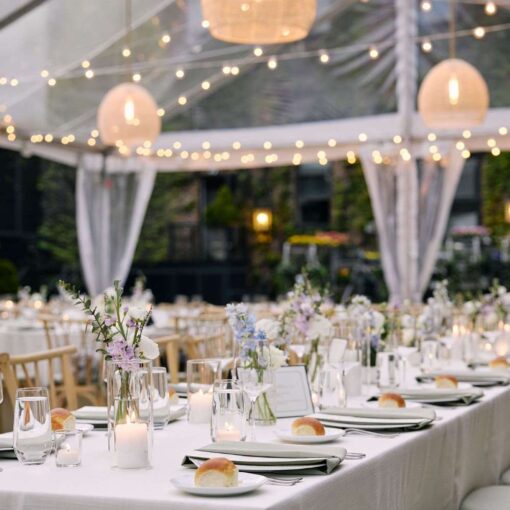 Rattan Lanterns hanging under a clear-top tent for Jocelyn & Andrew's wedding reception at The Foundry in Long Island City, NY. A clear tent with string lights, hosting a dinner party for many guests outside.