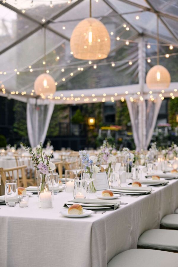Rattan Lanterns hanging under a clear-top tent for Jocelyn & Andrew's wedding reception at The Foundry in Long Island City, NY. A clear tent with string lights, hosting a dinner party for many guests outside.