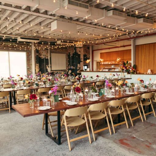 A long dinner table with florals set in The Corner Room at Rule of Thirds with warm white String Lights hanging overhead.
