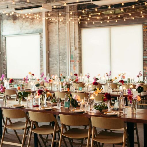A long dinner table with florals set in The Corner Room at Rule of Thirds with warm white String Lights hanging overhead.