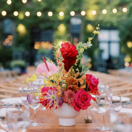 A red floral arrangement on a dinner table in the courtyard for Tina & Real's outdoor NYC wedding reception at The Foundry.