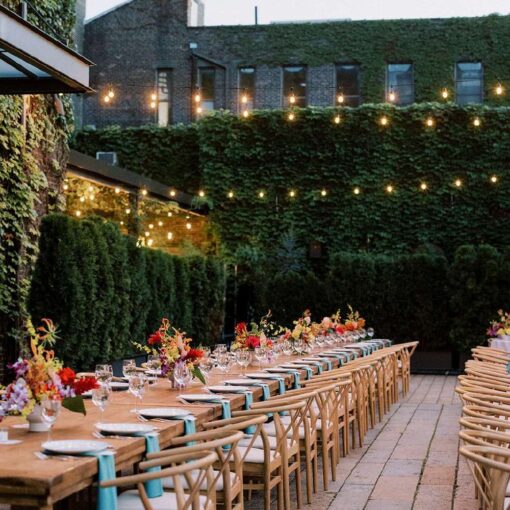 Dinner tables in the courtyard for Tina & Real's outdoor NYC wedding reception at The Foundry with String Lights hanging overhead.