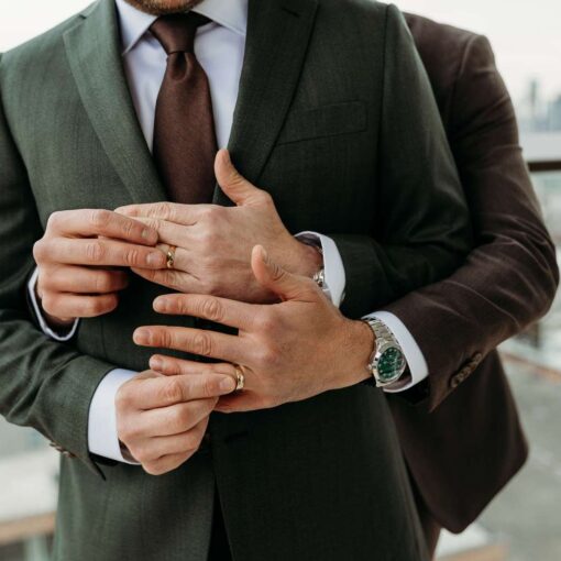 An intimate moment of affection, with a close-up of two formally dressed men sharing a tender embrace, highlighting their hands and wedding rings. An intimate moment of affection, with a close-up of two formally dressed men sharing a tender embrace, highlighting their hands and wedding rings.