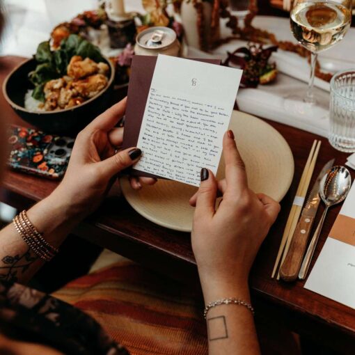 A wedding guest holding a card with a note, amidst a beautifully set table at Rule of Thirds. A wedding guest holding a card with a note, amidst a beautifully set table at Rule of Thirds.